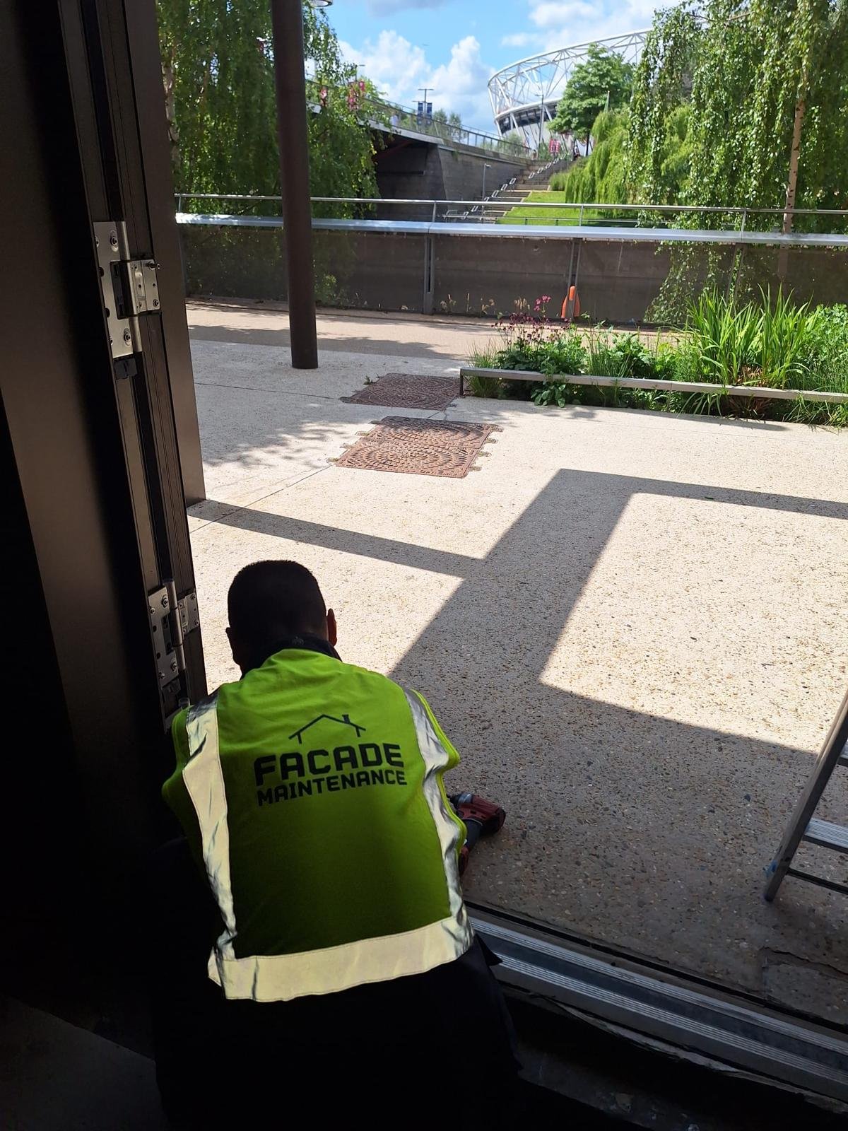 Technician working on a glazed door with a view to the London Stadium