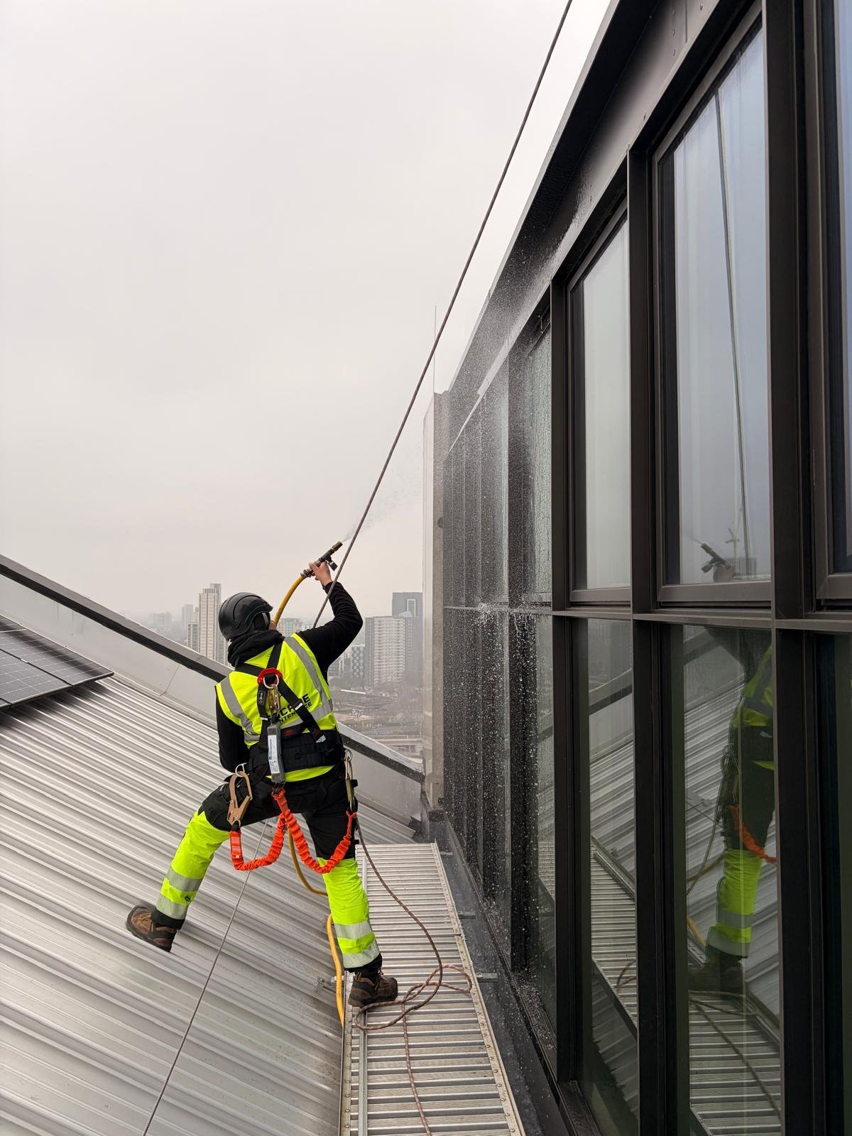 Facade Maintenance technician water-testing a glazed façade with a hose to trace water ingress